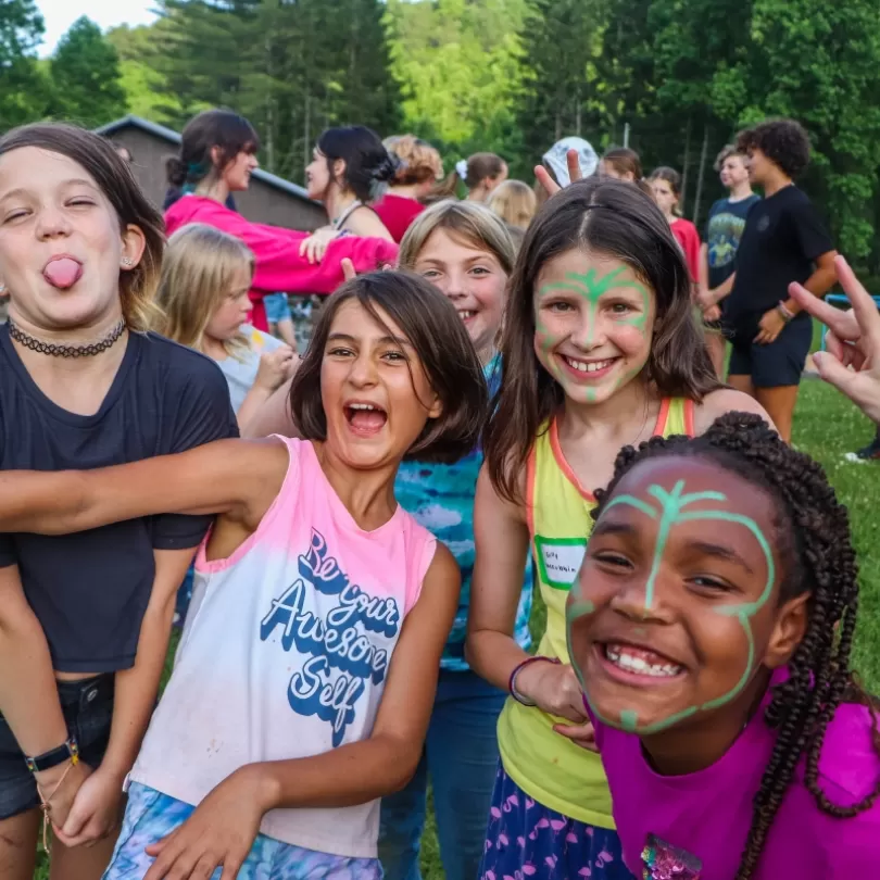 Multiple kids outside laughing and playing, smiling for the camera with face paint. Overnight camp