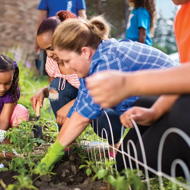 Several people of different generations have gloves on and are working in a garden together. 