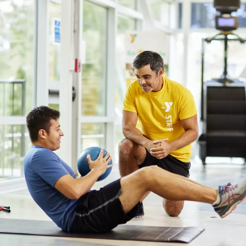 Man holding medicine ball and doing ab movement with personal trainer kneeling next to him coaching.