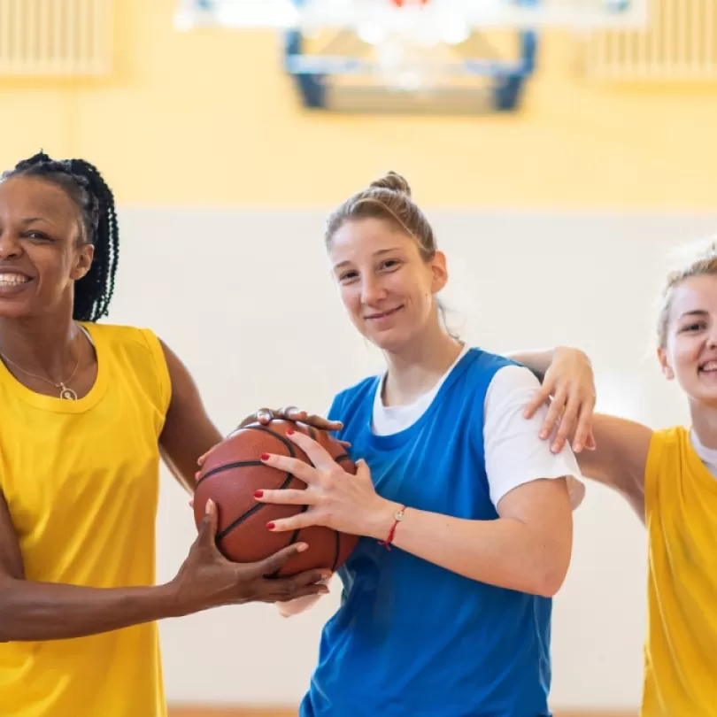 A group of adults play a game of basketball in gym.