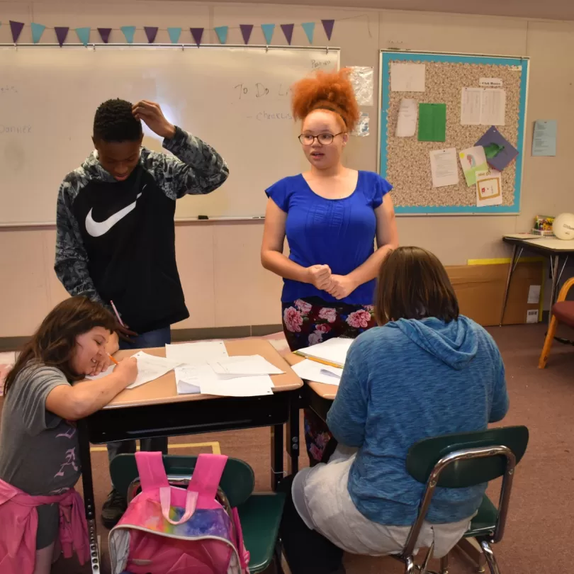 Four pre-teen looking kids work together on homework in a classroom setting.