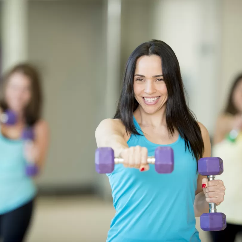 Woman with five pound weight holding up one weight in front, two other people behind are doing the same move 