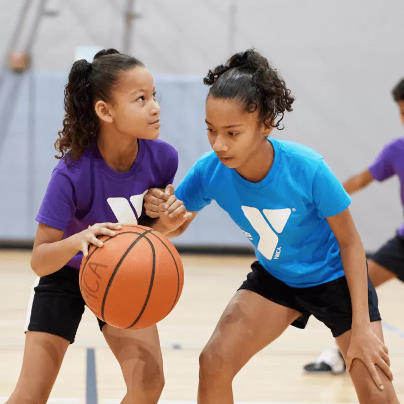 Two girls play basketball in a gym during a game.