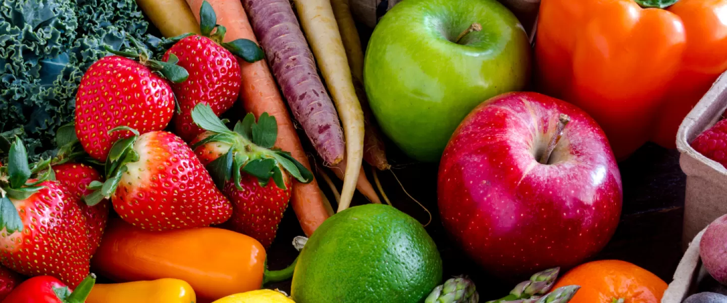 A flat lay of a large variety of fruits and vegetables. There are bell peppers, lemons, limes, apples, asparagus, tomatoes, berries, and carrots.