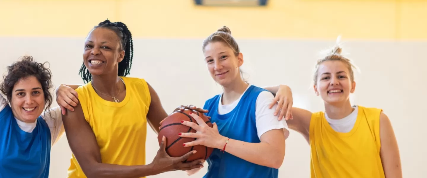 A group of adults play a game of basketball in gym.