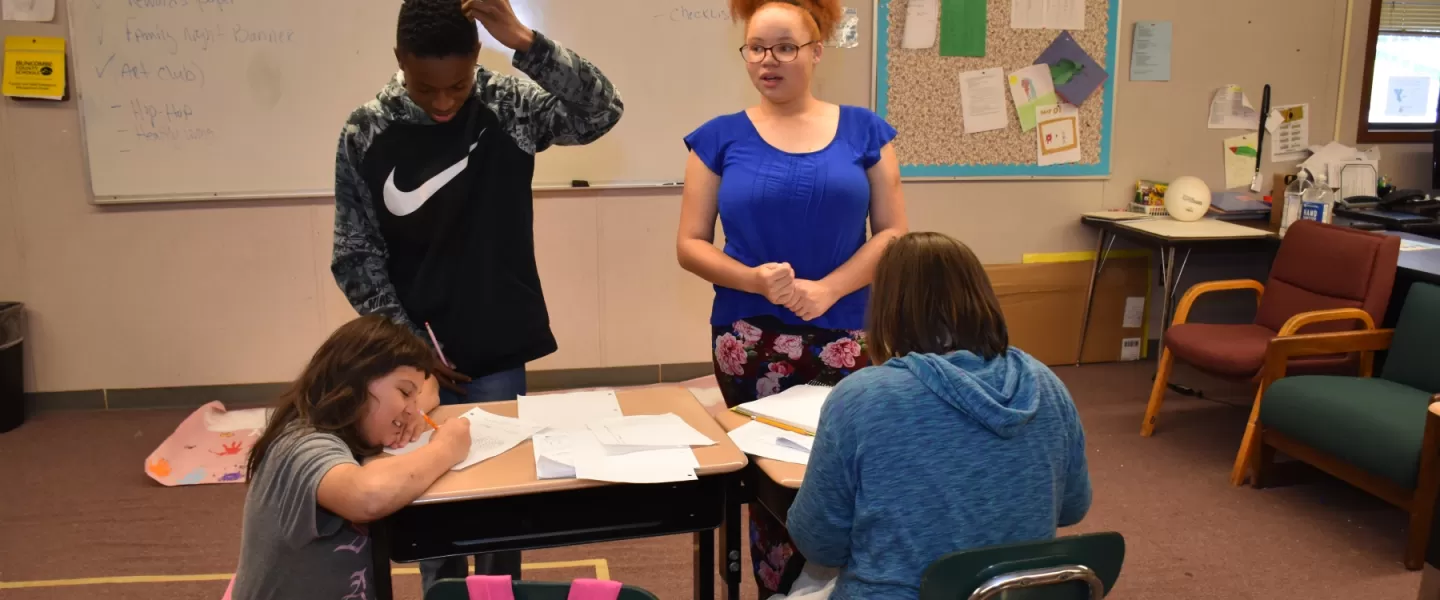 Four pre-teen looking kids work together on homework in a classroom setting.