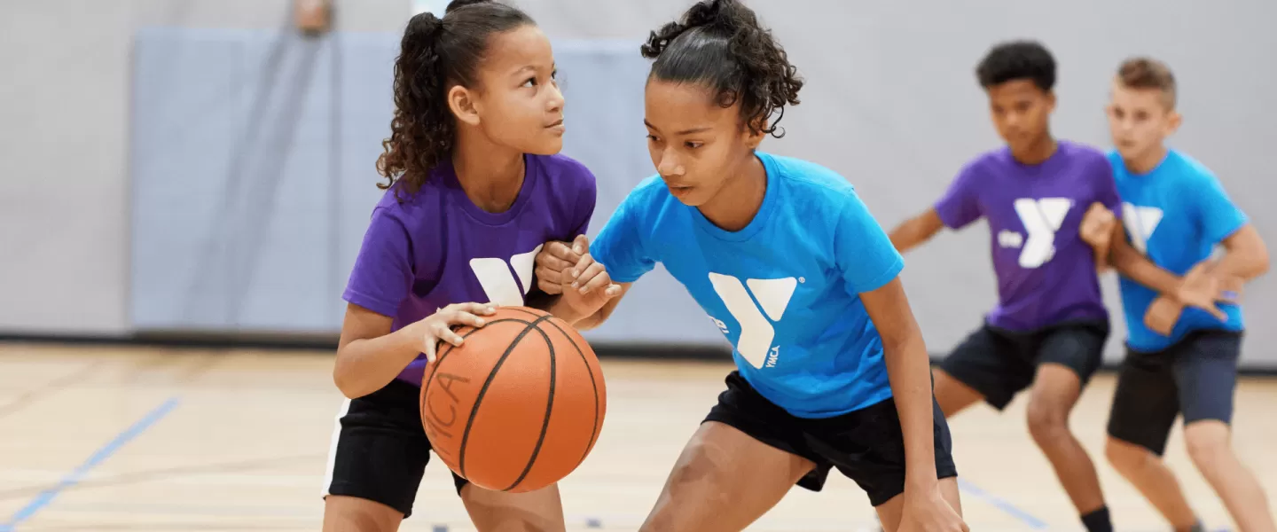 Two girls play basketball in a gym during a game.