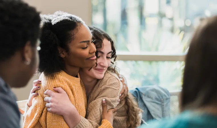 Two teenage girls hug each other as they sit in a teen support group session.