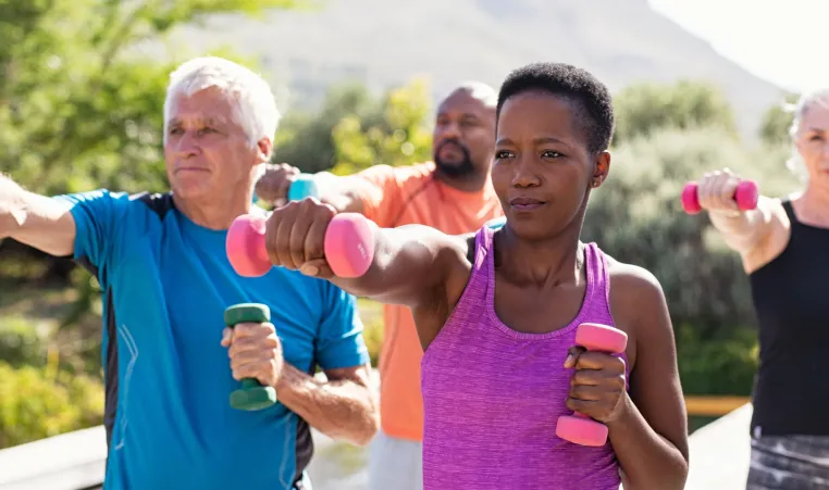 A group of older adults exercise and lift weights outside.