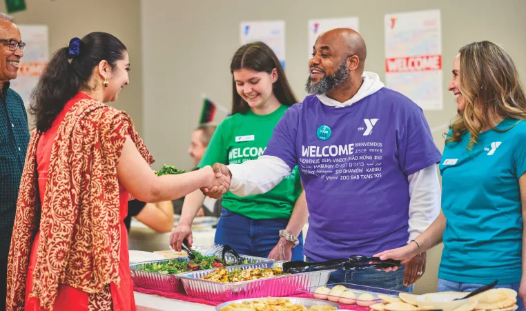 A man greets a woman at a Welcoming Week celebration at the YMCA.