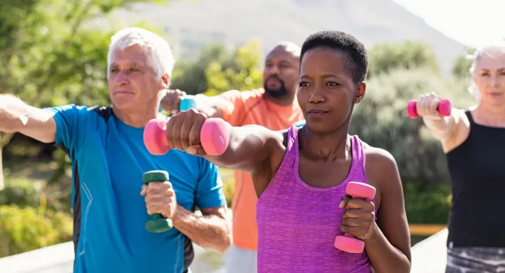 A group of older adults exercise and lift weights outside.