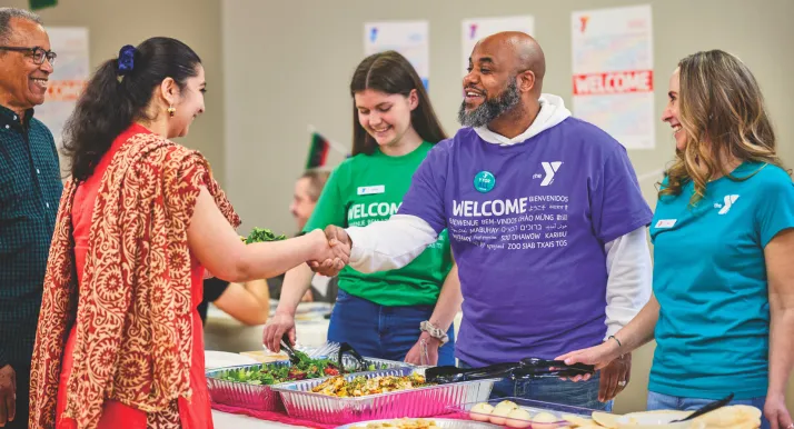 A man greets a woman at a Welcoming Week celebration at the YMCA.